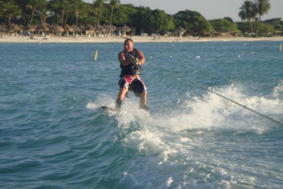 Man wakeboarding on a small wave. Palm trees and cabanas on the beach are in the background