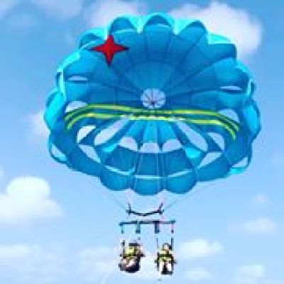 Two women parasailing with blue sail which has two yellow stripes and a red star on it