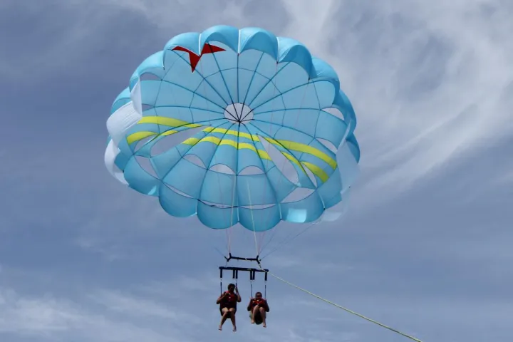 Two women parasailing with light blue sail